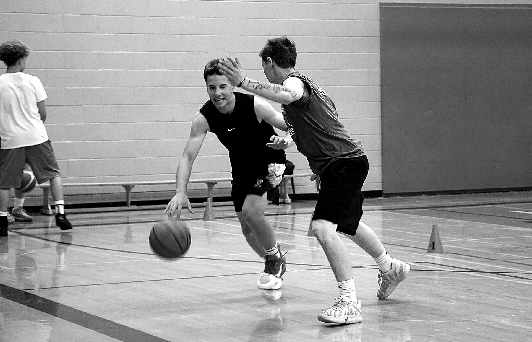 Two players go 1-on-1 in a gym, one driving left on the dribble